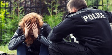 Police officer kneeling beside sitting teenage girl