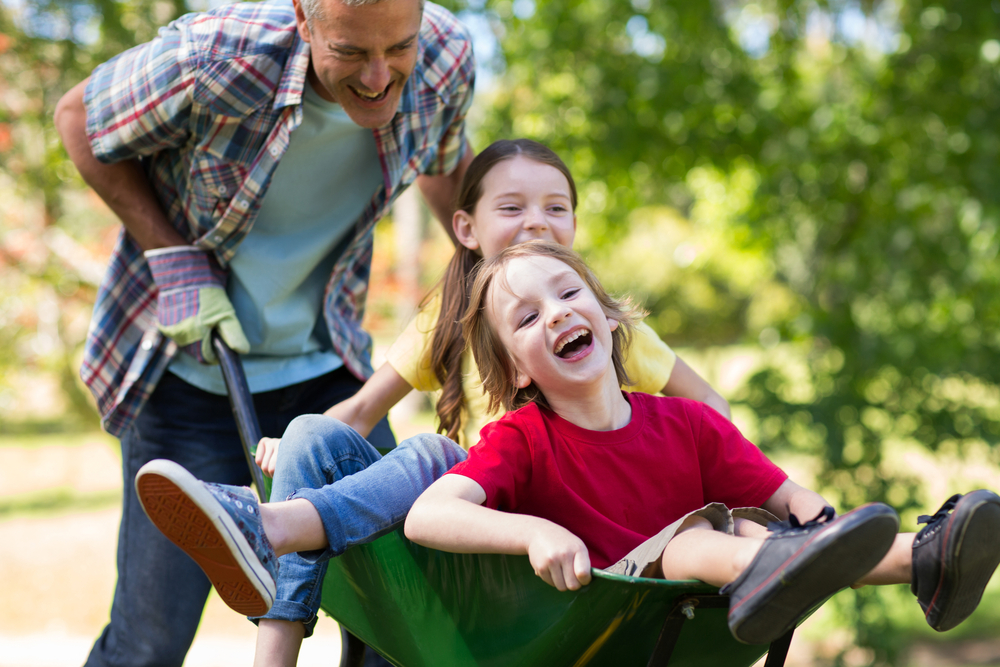 Happy father and his children playing with a wheelbarrow on a sunny day Happy father and his children playing with a wheelbarrow on a sunny day